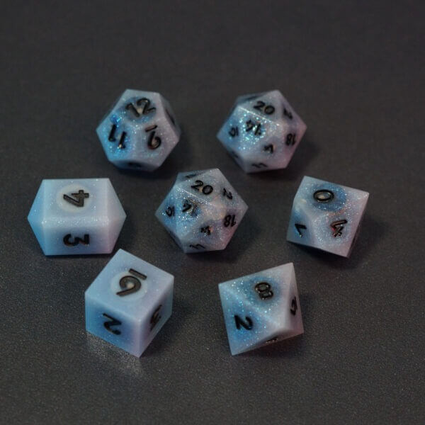 Set of 7 lit Aurora Sky dice with a rainbow of colors across all faces. Set Includes: 2 D20, 1 D12, 1 D10, 1 D8, 1 D6, 1 D4. Aurora Sky colorway is a mostly translucent white resin base packed with small blue and silver glitter throughout. The numbers or symbols are painted metallic black.