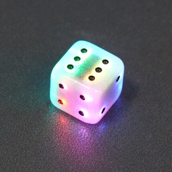 Collage of 7 lit Aurora Sky Pipped D6 with a rainbow of colors across each face. Aurora Sky colorway is a mostly translucent white resin base packed with small blue and silver glitter throughout. The numbers or symbols are painted metallic black.
