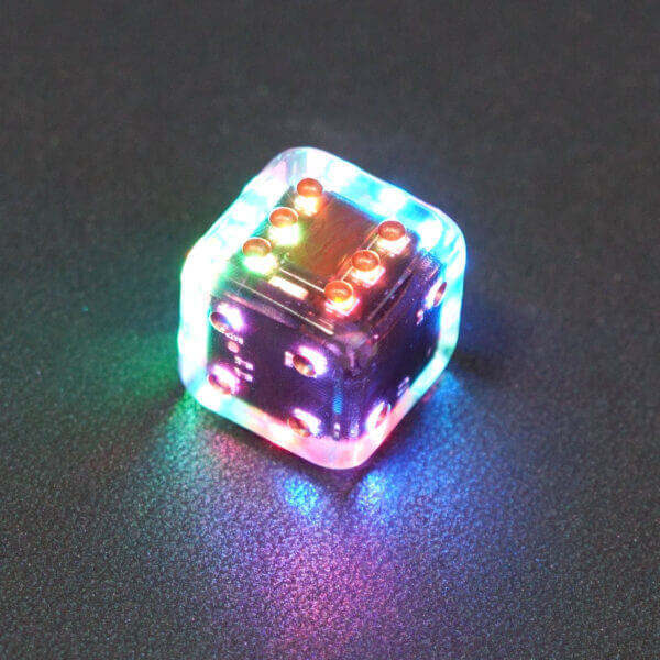 Collage of 7 lit Clear Pipped D6 with a rainbow of colors across each face. Clear colorway is fully transparent resin allowing internal circuit board to be visible. The numbers or symbols are painted metallic copper.