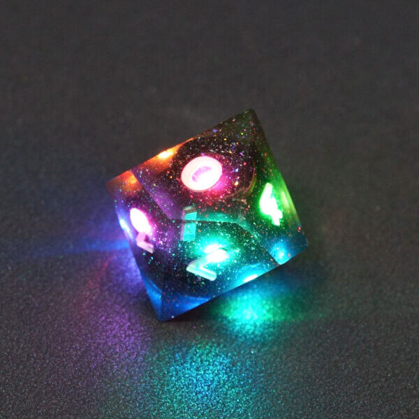Collage of 7 lit Midnight Galaxy D10 with a rainbow of colors across each face. Midnight Galaxy colorway is a mostly translucent dark smoke black resin base packed with rainbow glitter of various sizes. The numbers or symbols are painted pearl white.