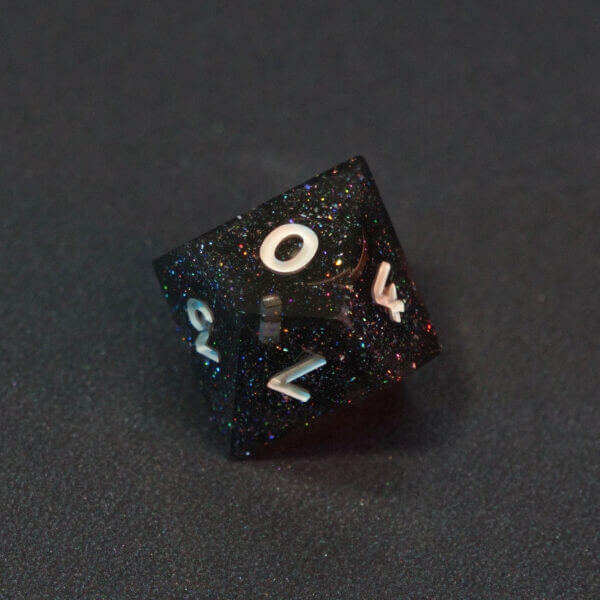 Collage of 7 lit Midnight Galaxy D10 with a rainbow of colors across each face. Midnight Galaxy colorway is a mostly translucent dark smoke black resin base packed with rainbow glitter of various sizes. The numbers or symbols are painted pearl white.