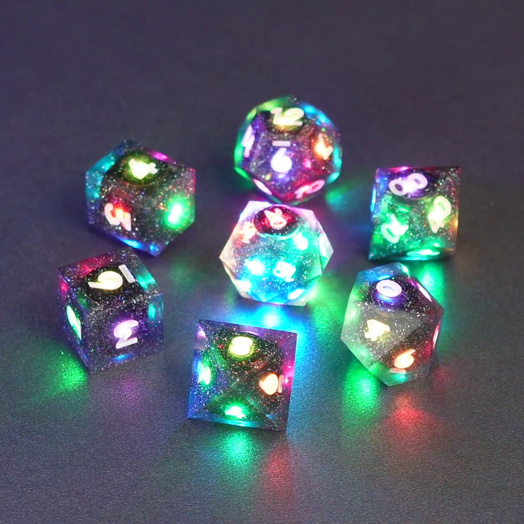 Set of 7 lit Midnight Galaxy dice with a rainbow of colors across all faces. Set Includes: 1 D20, 1 D12, 1 D00, 1 D10, 1 D8, 1 D6, 1 D4. Midnight Galaxy colorway is a mostly translucent dark smoke black resin base packed with rainbow glitter of various sizes. The numbers or symbols are painted pearl white.