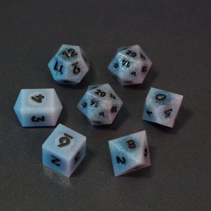 Set of 7 lit Aurora Sky dice with a rainbow of colors across all faces. Set Includes: 2 D20, 1 D12, 1 D10, 1 D8, 1 D6, 1 D4. Aurora Sky colorway is a mostly translucent white resin base packed with small blue and silver glitter throughout. The numbers or symbols are painted metallic black.