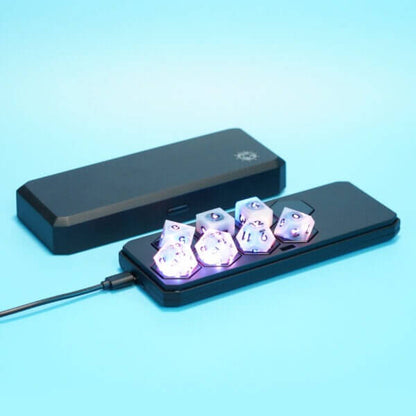 Set of 7 lit Aurora Sky dice with a rainbow of colors across all faces. Set Includes: 2 D20, 1 D12, 1 D10, 1 D8, 1 D6, 1 D4. Aurora Sky colorway is a mostly translucent white resin base packed with small blue and silver glitter throughout. The numbers or symbols are painted metallic black.