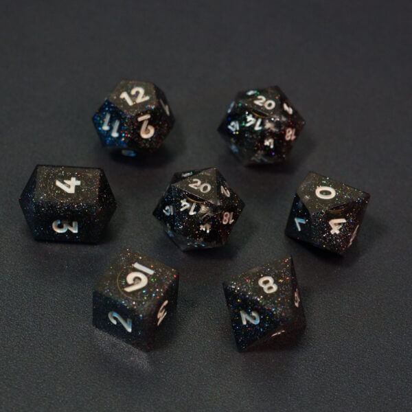 Set of 7 lit Midnight Galaxy dice with a rainbow of colors across all faces. Set Includes: 2 D20, 1 D12, 1 D10, 1 D8, 1 D6, 1 D4. Midnight Galaxy colorway is a mostly translucent dark smoke black resin base packed with rainbow glitter of various sizes. The numbers or symbols are painted pearl white.