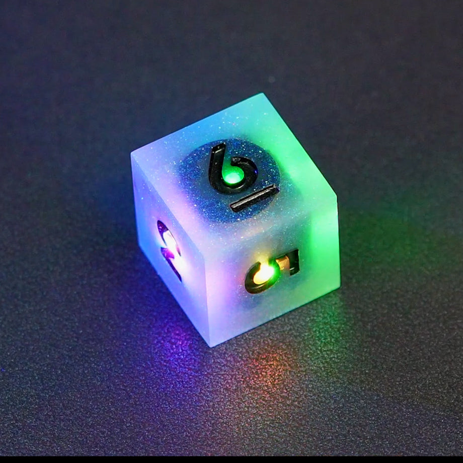 Lit Aurora Sky D6 with a rainbow of colors across each face. Aurora Sky colorway is a mostly translucent white resin base packed with small blue and silver glitter throughout. The numbers or symbols are painted metallic black.