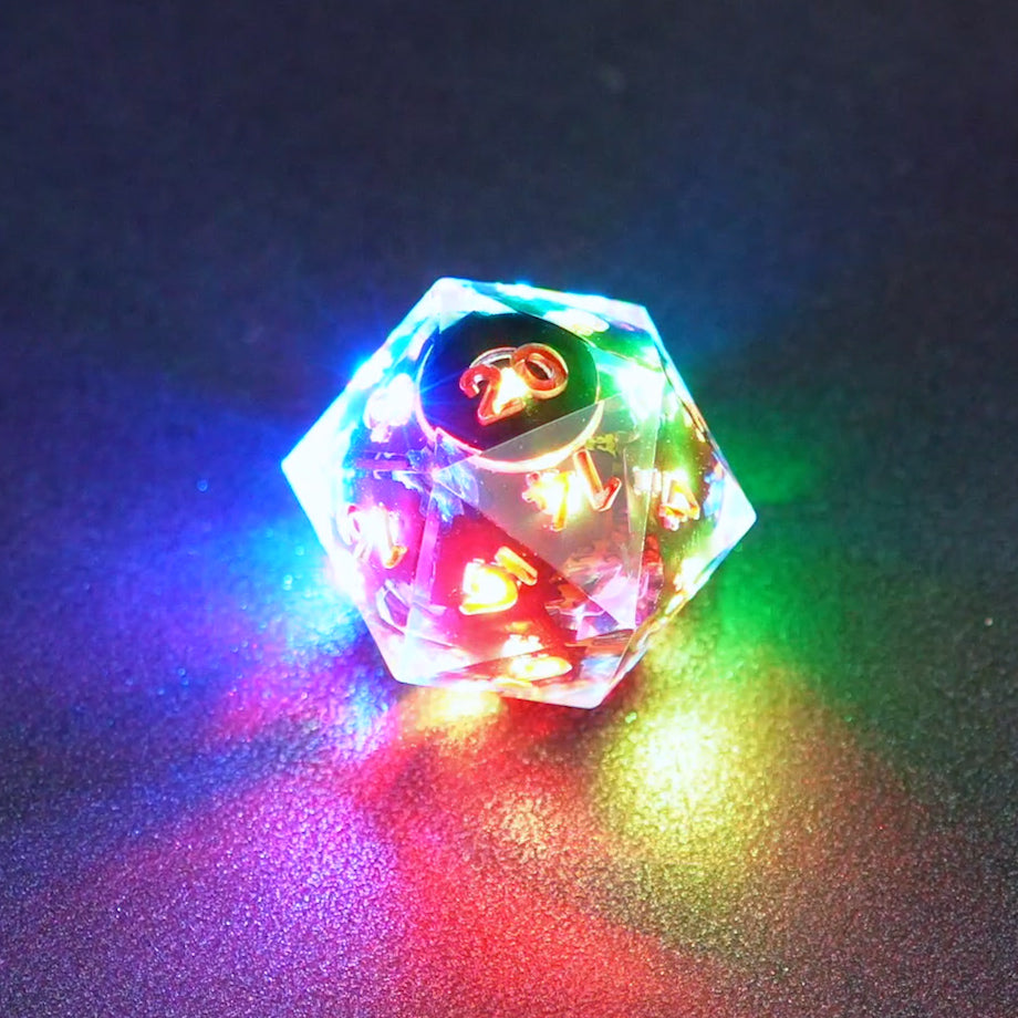 Lit Clear D20 with a rainbow of colors across each face. Clear colorway is fully transparent resin allowing internal circuit board to be visible. The numbers or symbols are painted metallic copper.