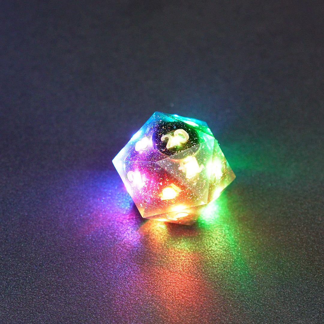 Lit Midnight Galaxy D20 with a rainbow of colors across each face. Midnight Galaxy colorway is a mostly translucent dark smoke black resin base packed with rainbow glitter of various sizes. The numbers or symbols are painted pearl white.