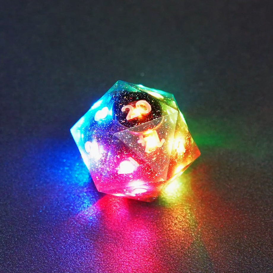 Lit Midnight Galaxy D20 with a rainbow of colors across each face. Midnight Galaxy colorway is a mostly translucent dark smoke black resin base packed with rainbow glitter of various sizes. The numbers or symbols are painted pearl white.