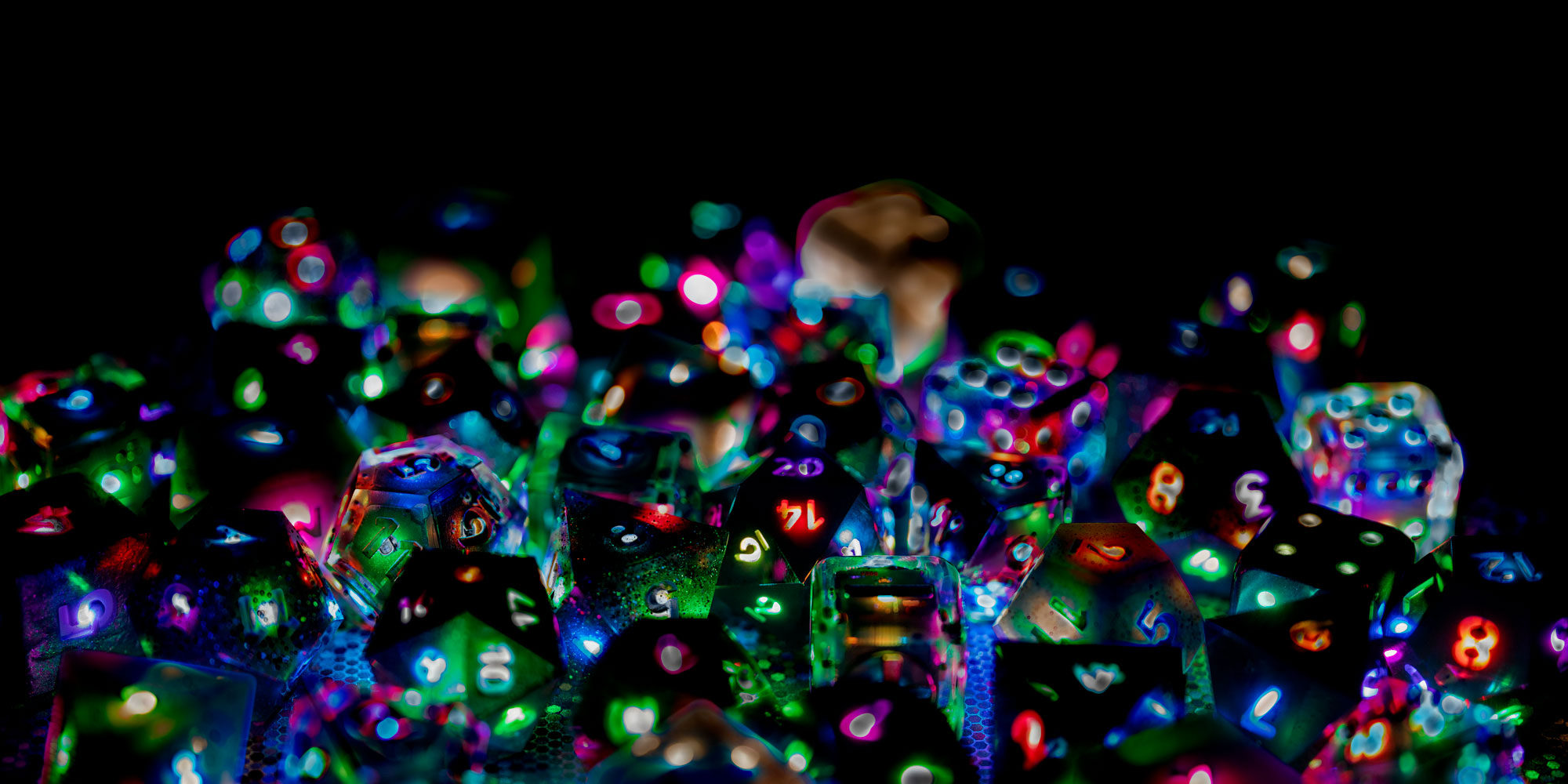 Photograph of a large pile of Pixels Dice in various colorways. All lights are on, shining a bright rainbow of colors through numbers and across faces.