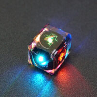 Lit Clear D4 in a crystal shape with a rainbow of colors across each face. Clear colorway is fully transparent resin allowing internal circuit board to be visible. The numbers or symbols are painted metallic copper.