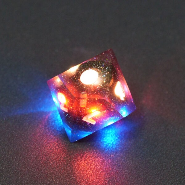 Lit Midnight Galaxy D10 with red and blue colors across each face. Midnight Galaxy colorway is a mostly translucent dark smoke black resin base packed with rainbow glitter of various sizes. The numbers or symbols are painted pearl white.