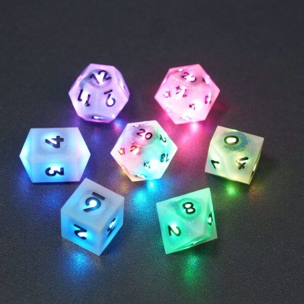 Set of 7 lit Aurora Sky dice with a rainbow of colors across all faces. Set Includes: 2 D20, 1 D12, 1 D10, 1 D8, 1 D6, 1 D4. Aurora Sky colorway is a mostly translucent white resin base packed with small blue and silver glitter throughout. The numbers or symbols are painted metallic black.