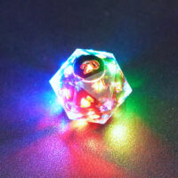 Lit Clear D20 with a rainbow of colors across each face. Clear colorway is fully transparent resin allowing internal circuit board to be visible. The numbers or symbols are painted metallic copper.