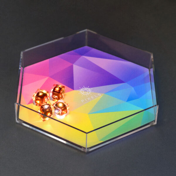 Lit Clear D6s in a hex-shaped clear acrylic dice tray. Tray has a mat with a bright rainbow abstract design and Pixels logo in the center.