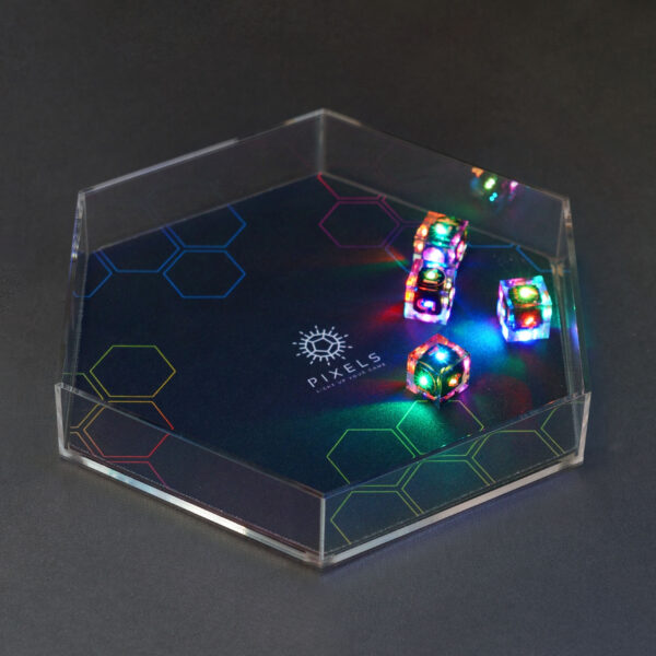 Lit Clear D6s in a hex-shaped clear acrylic dice tray. Tray has a mat with a black and rainbow hex design and Pixels logo in the center.