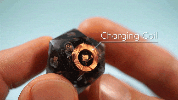 GIF of hands turning a clear D20 that has callouts for internal components Charging Coil, LED, and Counterweight.