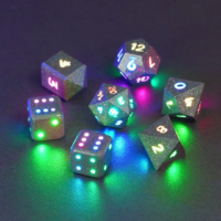Set of 7 lit Hematite Grey dice with a rainbow of colors across all faces. Set Includes: 1 D20, 1 D12, 1 D10, 1 D8, 2 Pipped D6, 1 D4. Hematite Grey colorway is a fully opaque medium tone silver resin packed with rainbow glitter of various sizes. The numbers or symbols are painted pale white.