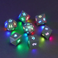 Set of 7 lit Hematite Grey dice with a rainbow of colors across all faces. Set Includes: 1 D20, 1 D12, 1 D00, 1 D10, 1 D8, 1 D6, 1 D4. Hematite Grey colorway is a fully opaque medium tone silver resin packed with rainbow glitter of various sizes. The numbers or symbols are painted pale white.