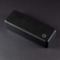 Large Charging Case - closed. A rectangular shaped black box with a silver Pixels logo in one corner on the lid. The lid has a button on a long edge to unlatch from the bottom half of the case.