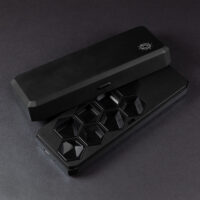 Large Charging Case - opened. A rectangular shaped black box with a silver Pixels logo in one corner on the lid. The lid has a button on a long edge to unlatch from the bottom half of the case. The bottom has eight hex-shaped slots with dice trays in place for an RPG set - seven standard dice and a blank.