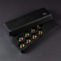 Large Charging Case - opened. A rectangular shaped black box with a silver Pixels logo in one corner on the lid. The lid has a button on a long edge to unlatch from the bottom half of the case. The bottom has eight hex-shaped slots for dice trays which are empty showing copper wireless charging coils.