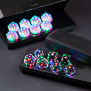 Photograph of two sets of Pixels Dice in black Large Charging Cases. The dice are a Clear RPG set and Aurora Sky D20 set. All dice are lit a rainbow of colors from within.